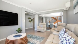 Un salon moderne avec un téléviseur à écran plat, un canapé beige, un tapis à motifs et une table basse en bois.