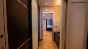 A hallway with wooden flooring, a door on the right, and a kitchen visible in the background. - Navy Apartment by Wonderful Italy (Bari)
