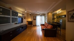 A modern living room with a sofa, a TV, and a fireplace. There is a kitchen area with a refrigerator and a dining table. - Navy Apartment by Wonderful Italy (Bari)