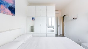 A modern bedroom with a large bed, a wardrobe, a mirror, and a painting on the wall.