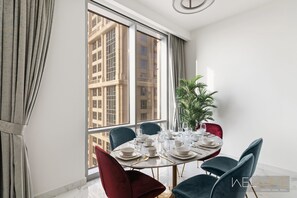 A dining area with a round table set for six, large windows, and a potted plant.
