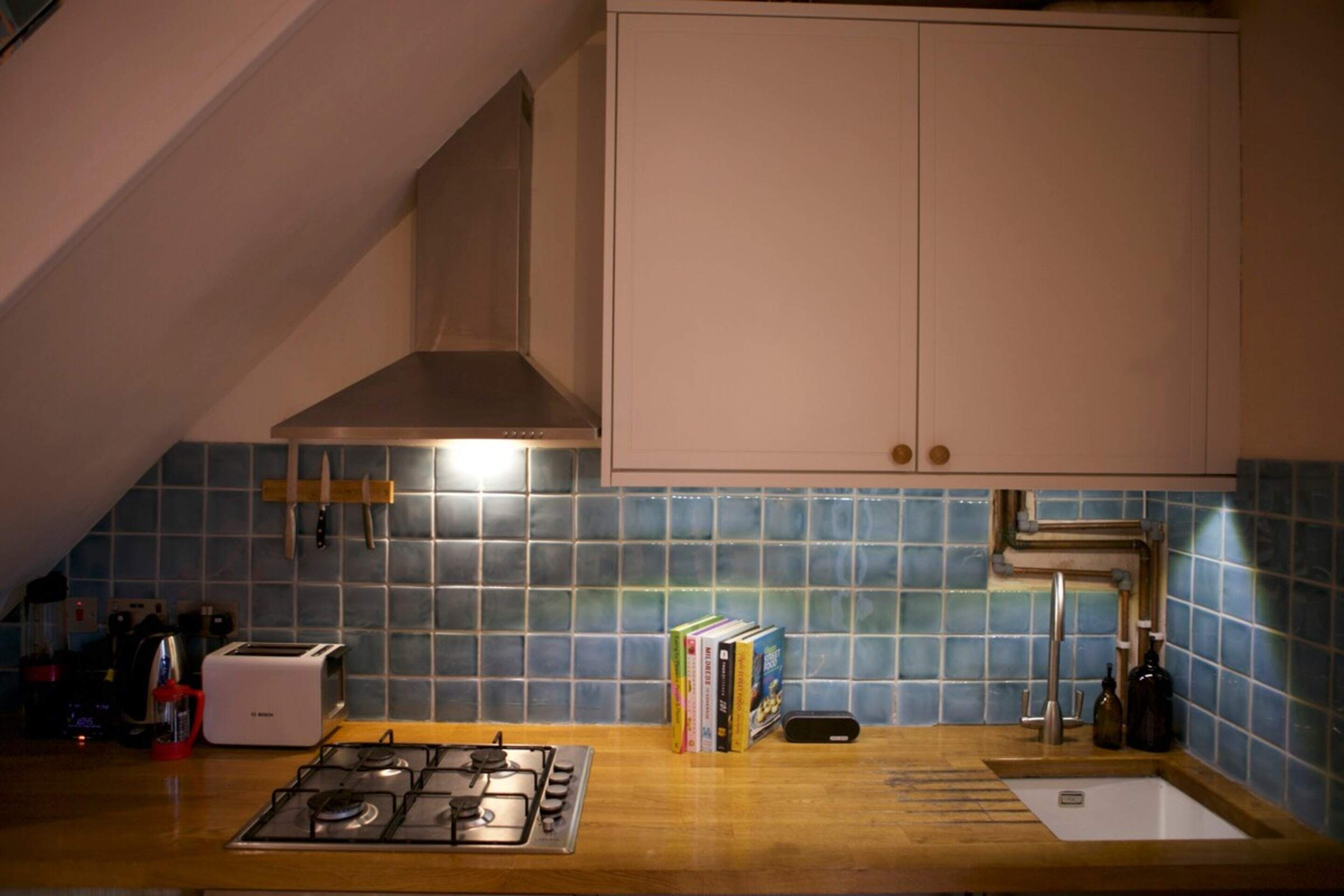 A kitchen with a gas stove, a toaster, a sink, and a range hood.