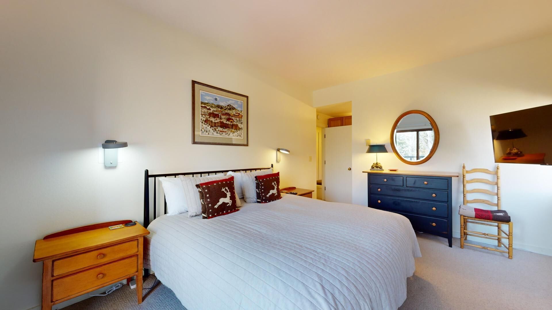 Une chambre à coucher avec un grand lit, des tables de chevet, une commode, une chaise, un miroir et un tableau accroché au mur.