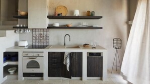 Uma cozinha compacta com forno embutido, lava-louças e pia. Prateleiras acima do balcão exibem diversos utensílios de cozinha.