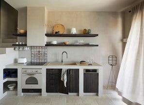 A compact kitchen with a built-in oven, a dishwasher, and a sink. There are shelves above the counter holding various kitchen items.