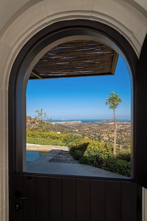 An arched doorway leading to a balcony with a view of a hilly landscape and a clear blue sky.