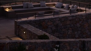 Um terraço no telhado com muro de pedra, sofá com almofadas e vista para montanhas ao longe.