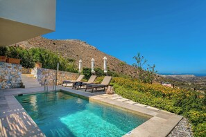 A swimming pool with lounge chairs, stone steps, and a view of a hillside.