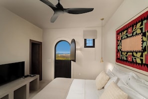 A bedroom with a bed, a TV, a ceiling fan, a door, a window, and a view of the landscape.