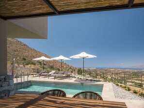 A pool with lounge chairs and umbrellas, overlooking a mountainous landscape.