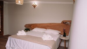 A neatly made bed with white linens and towels, a small bedside table with a plant, and a unique wooden headboard. - Recanto das Videiras (Itapira)