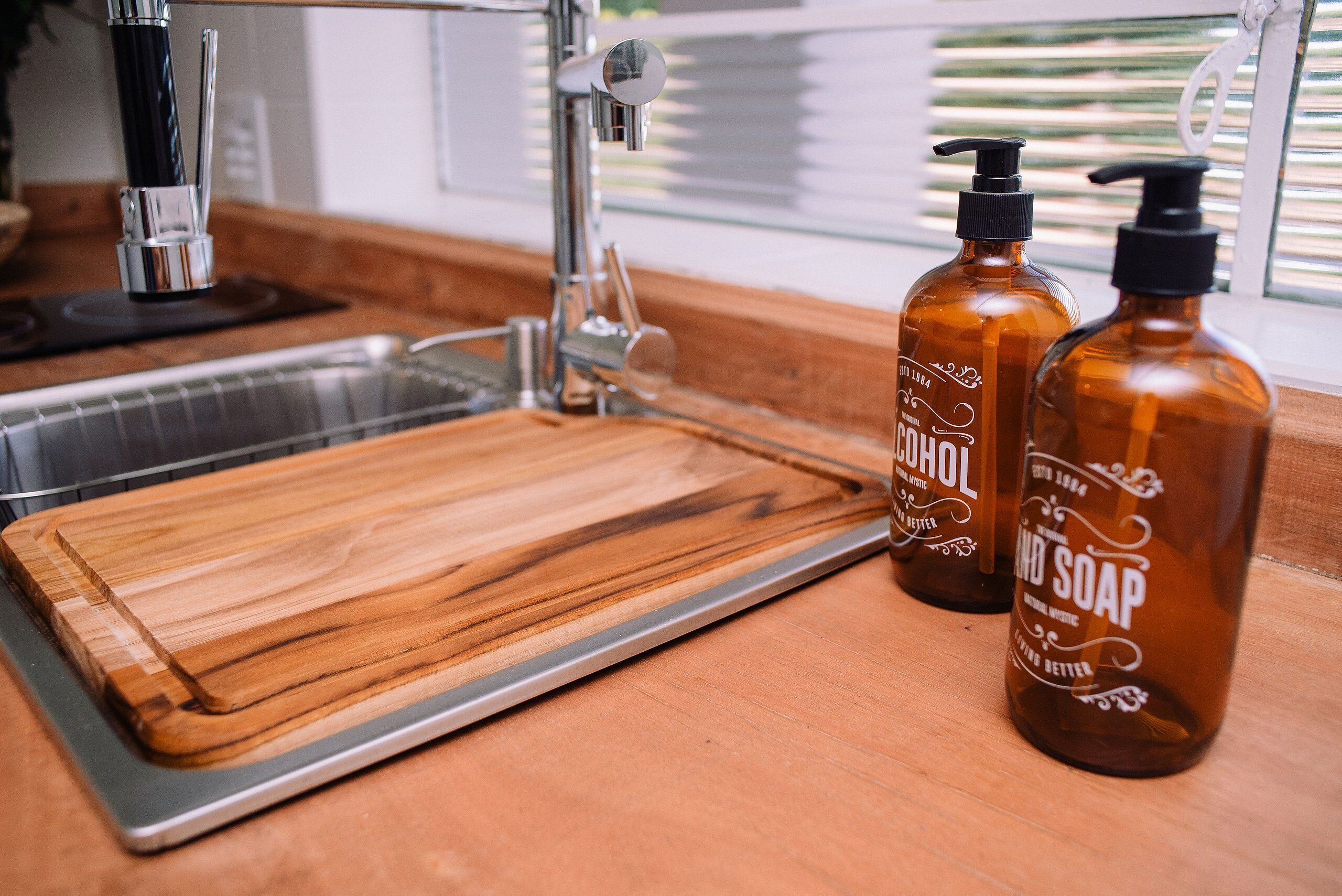 A kitchen counter with a wooden cutting board, a stainless steel sink, and two bottles of hand soap.