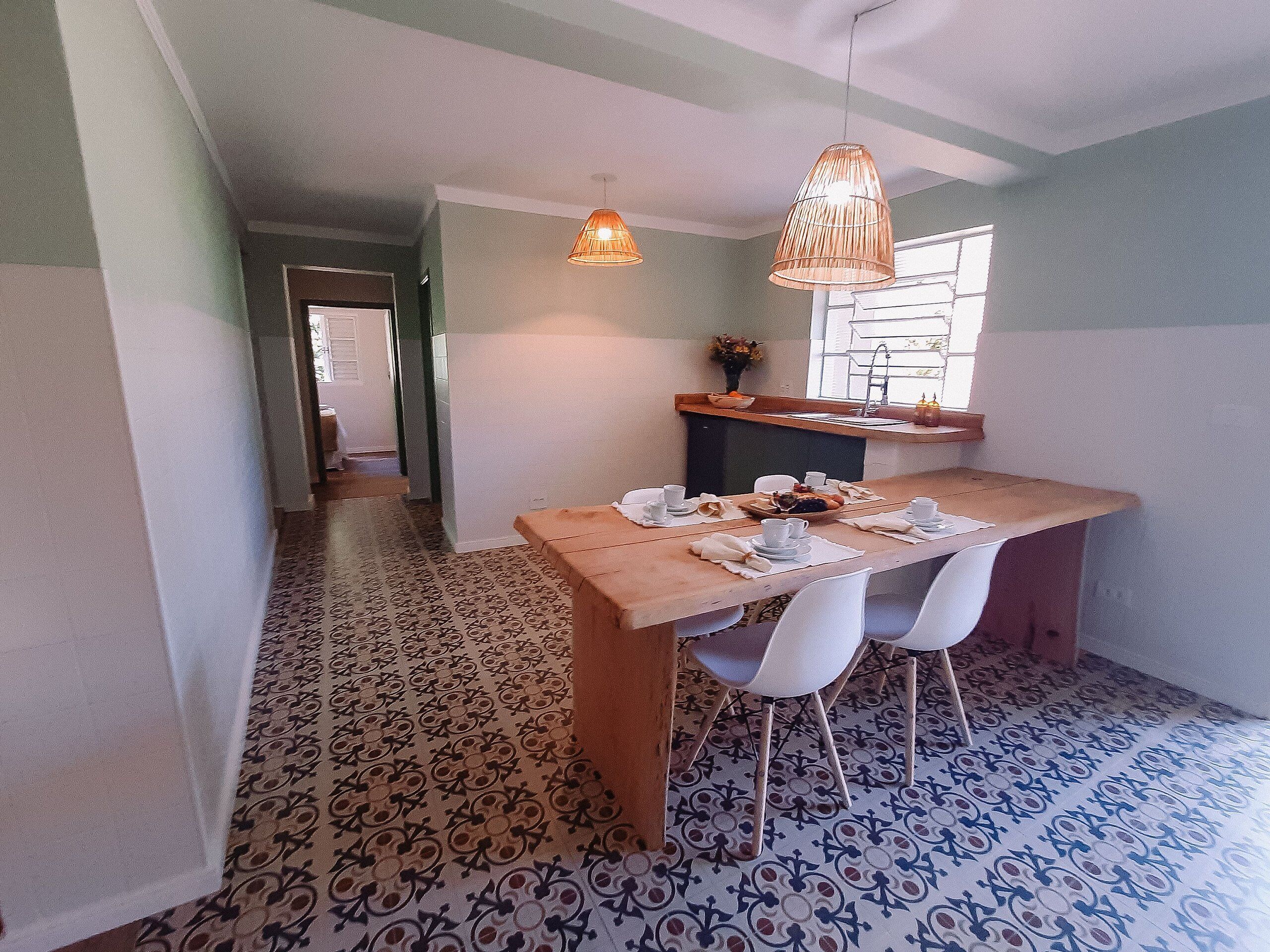 A dining area with a wooden table set for four, a hanging light fixture, and patterned floor tiles.
