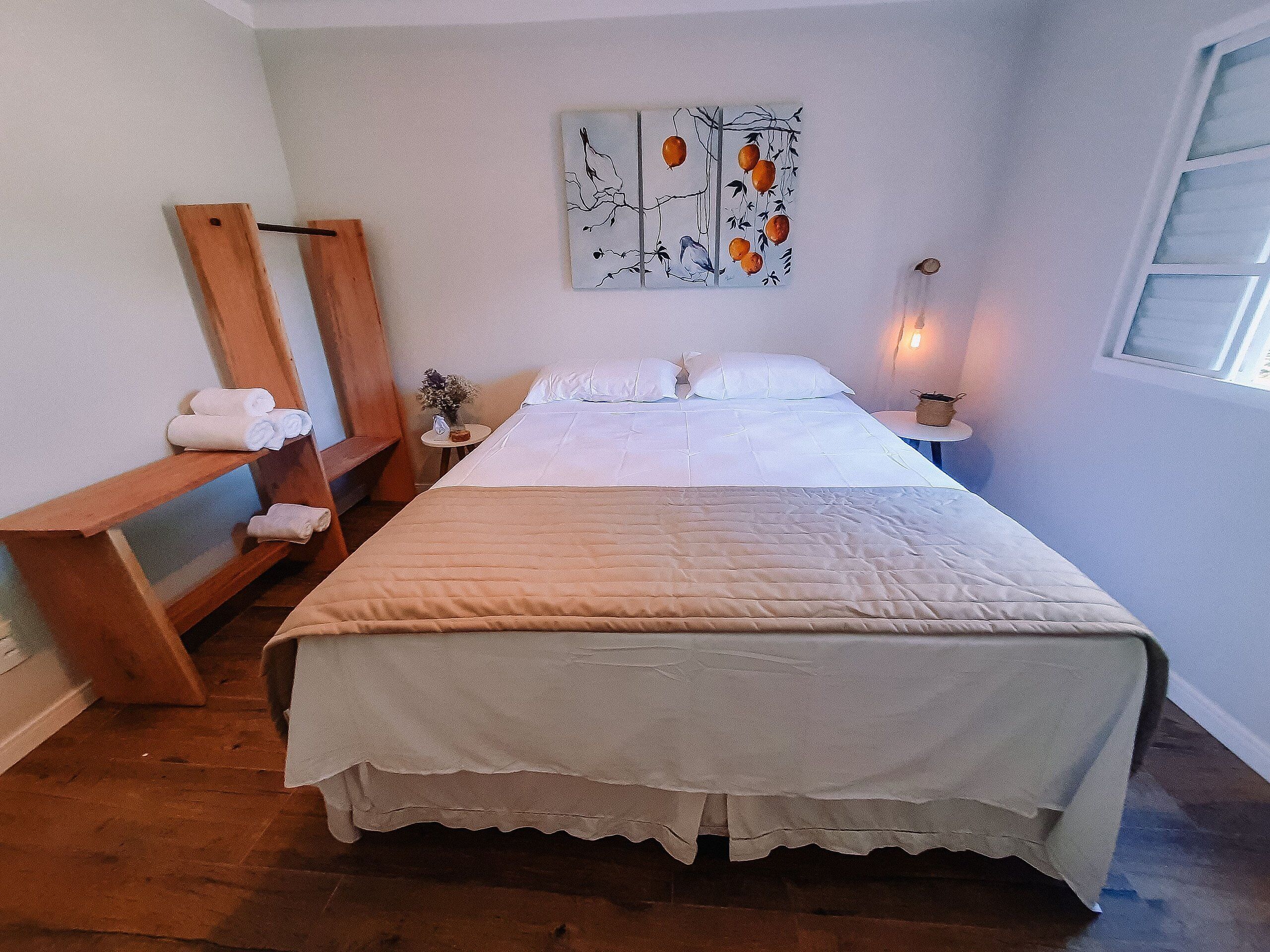 Una cama bien tendida con una colcha blanca y un banco de madera con toallas a un lado.