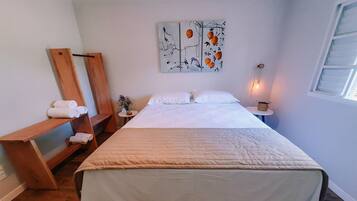 Una cama bien tendida con una colcha blanca y un banco de madera con toallas a un lado.