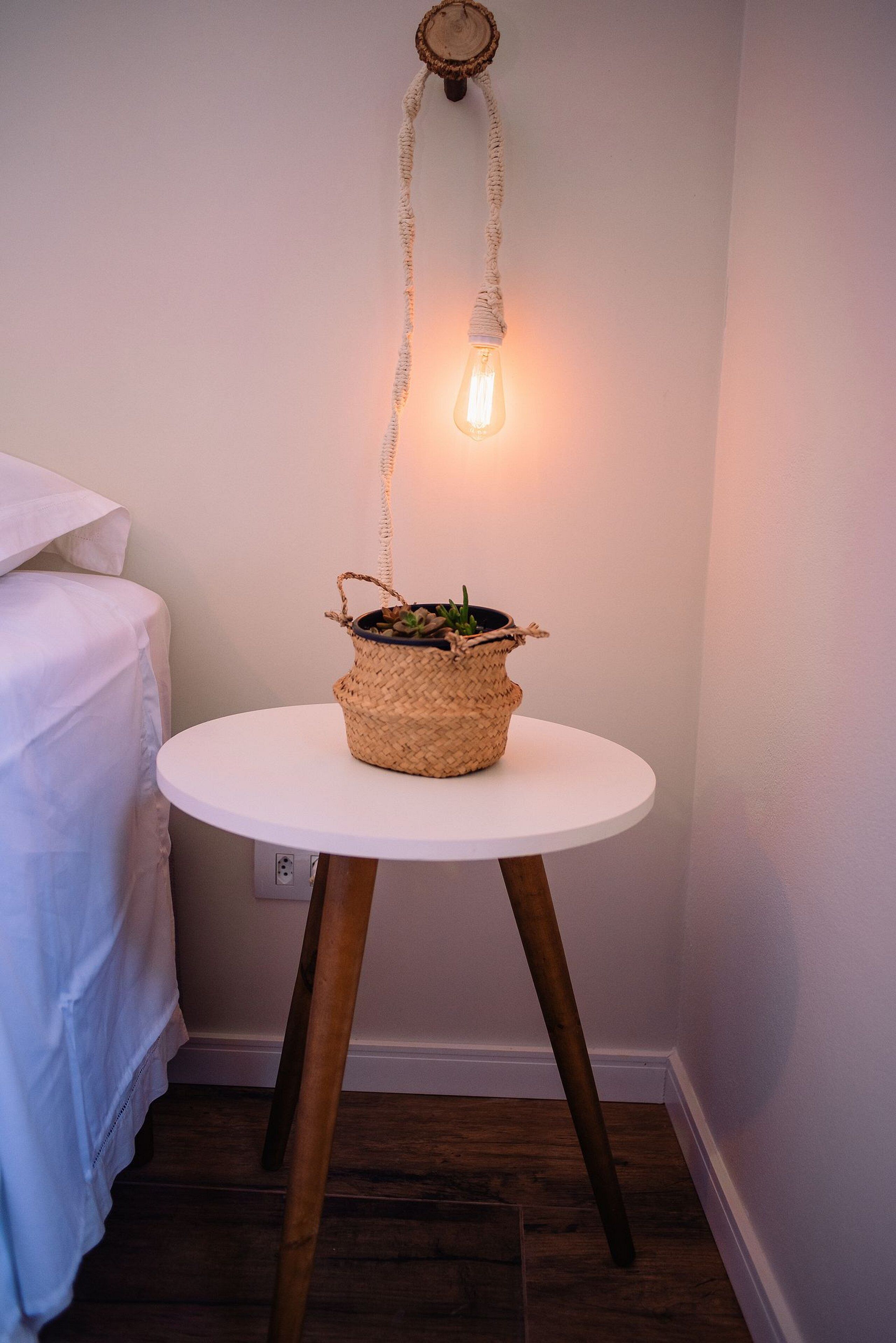 A small round table with a woven basket containing a plant, positioned against a wall with a hanging light fixture.