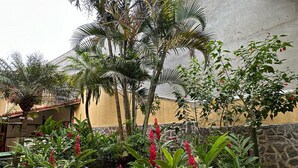 A courtyard with a variety of tropical plants, a stone wall, and a tiled floor. - Pousada Via Mar Buzios (Búzios)