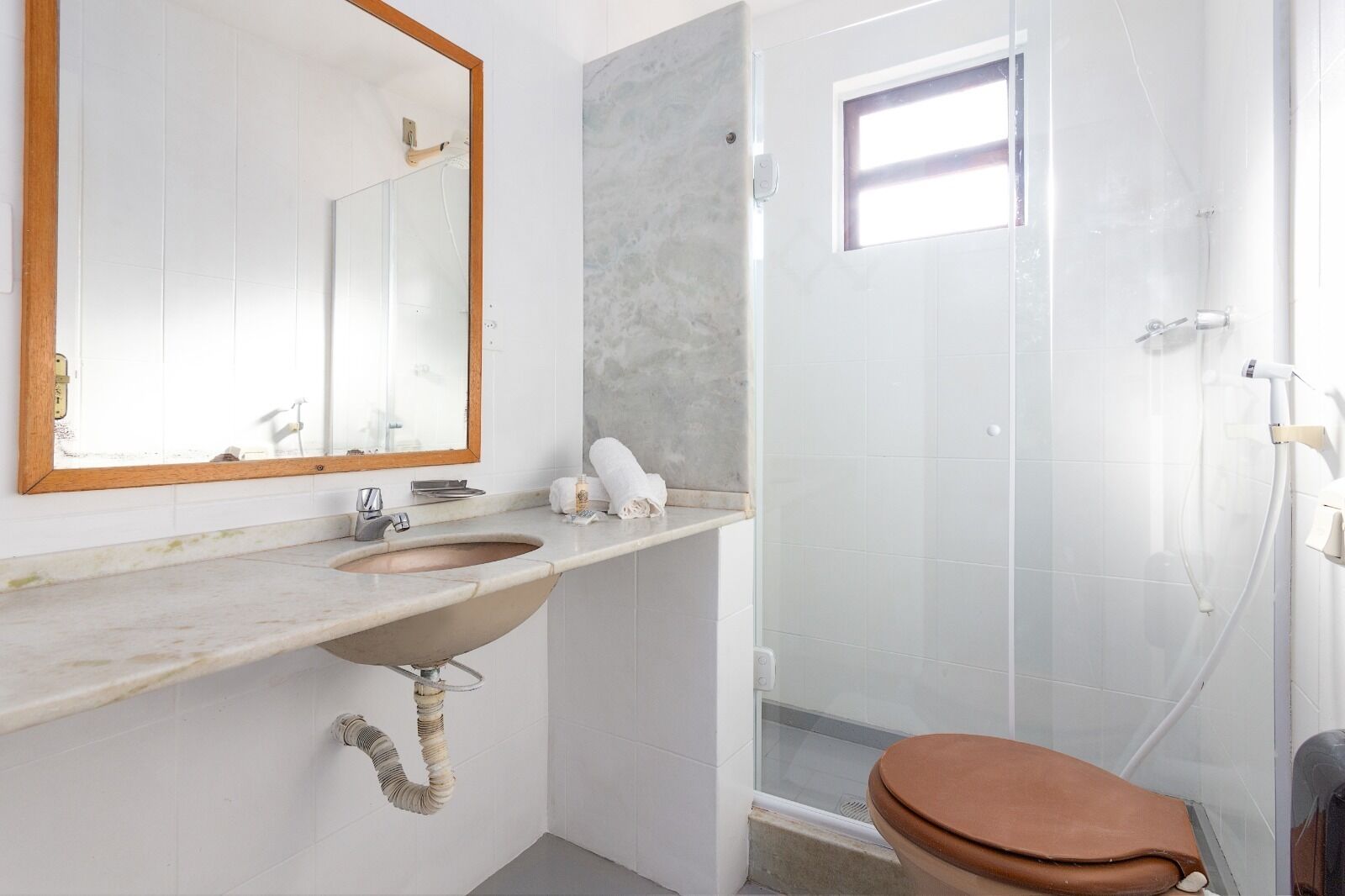 Une salle de bain avec un lavabo en marbre, un miroir encadré en bois, des toilettes et une douche séparée par une paroi en verre.