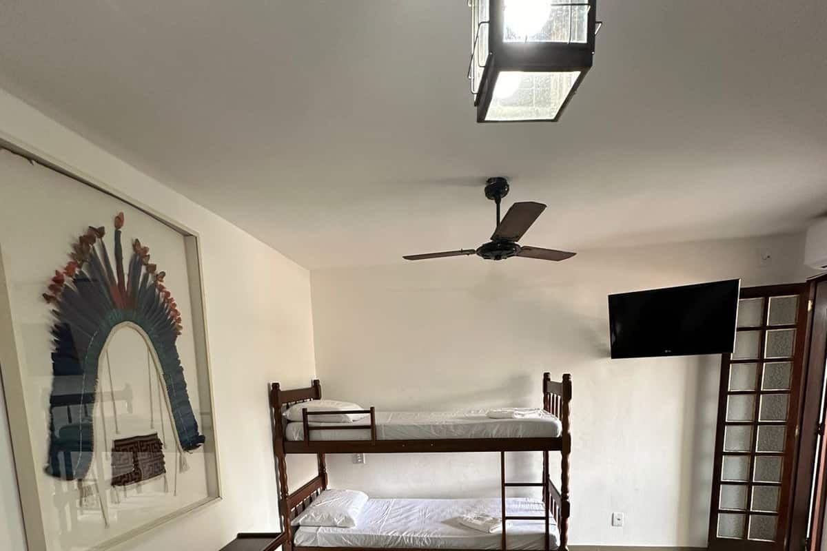 A room with a bunk bed, a single bed, a ceiling fan, a TV, and a framed artwork on the wall.