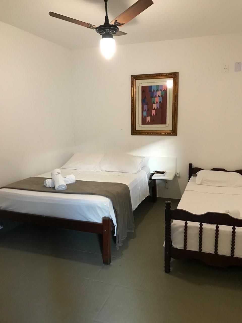 A hotel room with two beds, a ceiling fan, a framed artwork on the wall, and a bedside table with a lamp.