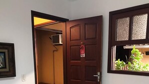A hotel room with two single beds, a wooden door, a small window with a view of greenery, and a framed picture on the wall. - Pousada Via Mar Buzios (Búzios)
