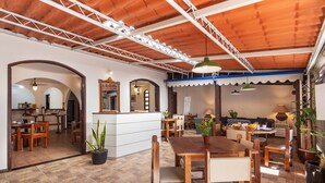 A spacious dining area with wooden tables and chairs, a reception desk, and a tiled floor. - Pousada Via Mar Buzios (Búzios)
