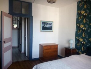 Una camera da letto con un letto, una cassettiera, un comodino, una porta che dà su un corridoio e un quadro appeso alla parete.