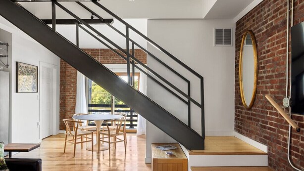 A modern interior with a staircase, wooden flooring, a dining area, and a brick wall.