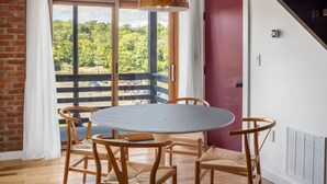 A room with a large window, a round table with chairs, and a hanging pendant light.