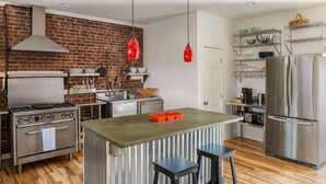 A modern kitchen with a brick wall, stainless steel appliances, and a central island with stools.