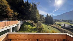 Una terraza de madera con vistas a una ladera verde y un pueblo a lo lejos.