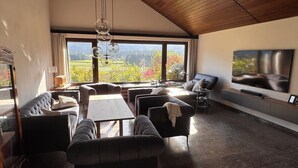 Amplia sala de estar con techo alto, ventanas grandes que ofrecen vistas a un paisaje montañoso, un televisor de pantalla plana montado en la pared y una zona de estar acogedora con sofás y una mesa de centro.