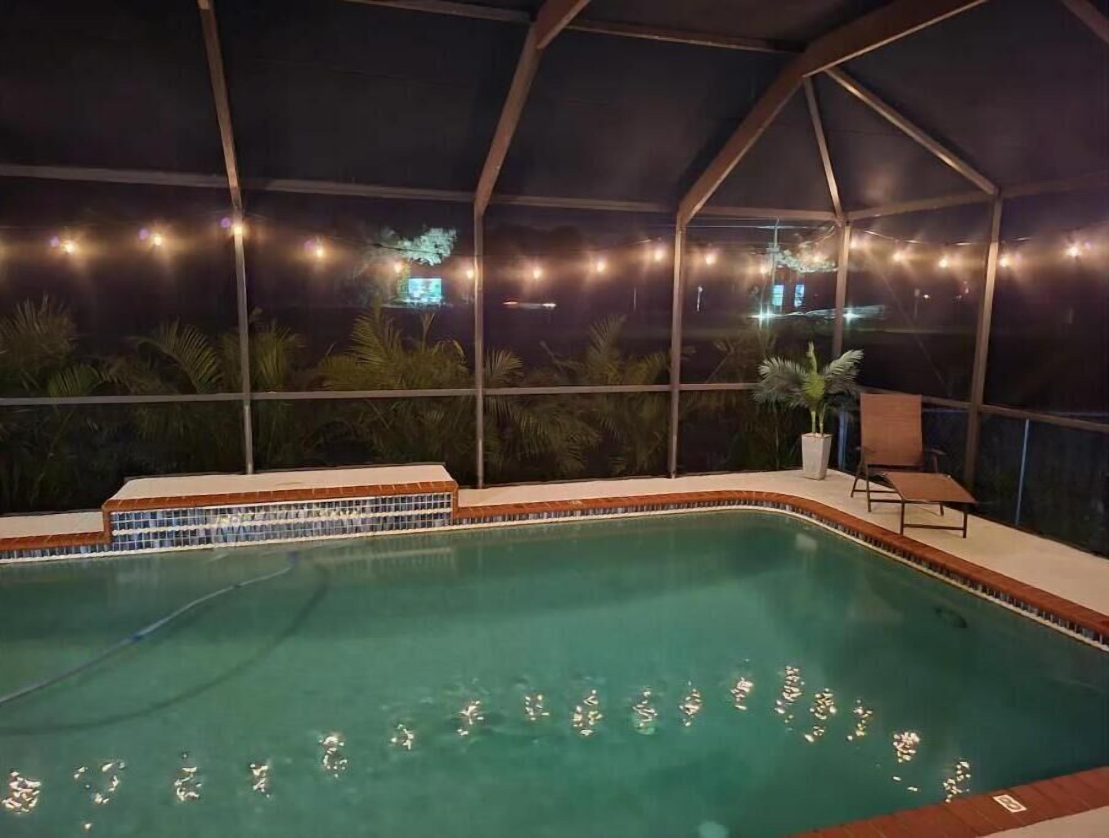 An indoor swimming pool with a tiled edge, surrounded by a glass enclosure with string lights.