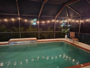 Piscina interior com borda azulejada, cercada por um envidraçamento com luzes de cordão.