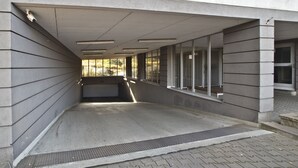 Ein überdachter Außenbereich mit Betonboden, Metallgeländern und Blick auf ein Gebäude im Hintergrund.