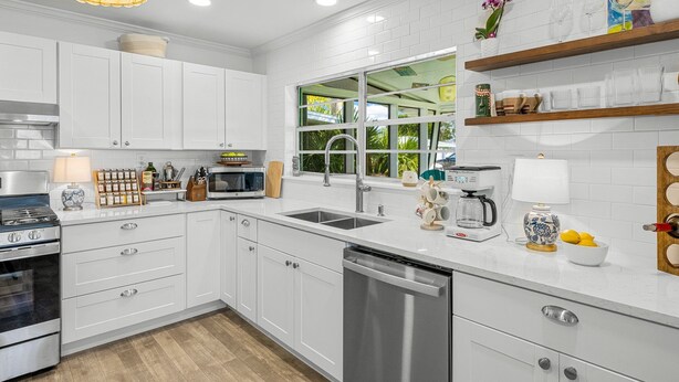 A modern kitchen with white cabinets, stainless steel appliances, a window with a view, and a decorative shelf with items.
