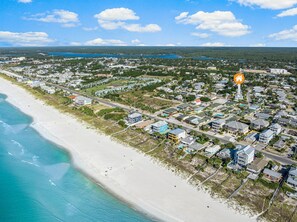An aerial view of a coastal town with a beach, houses, and a road.