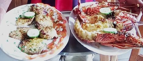 Two plates of seafood dishes, possibly lobster and fish, garnished with slices of cucumber and herbs.