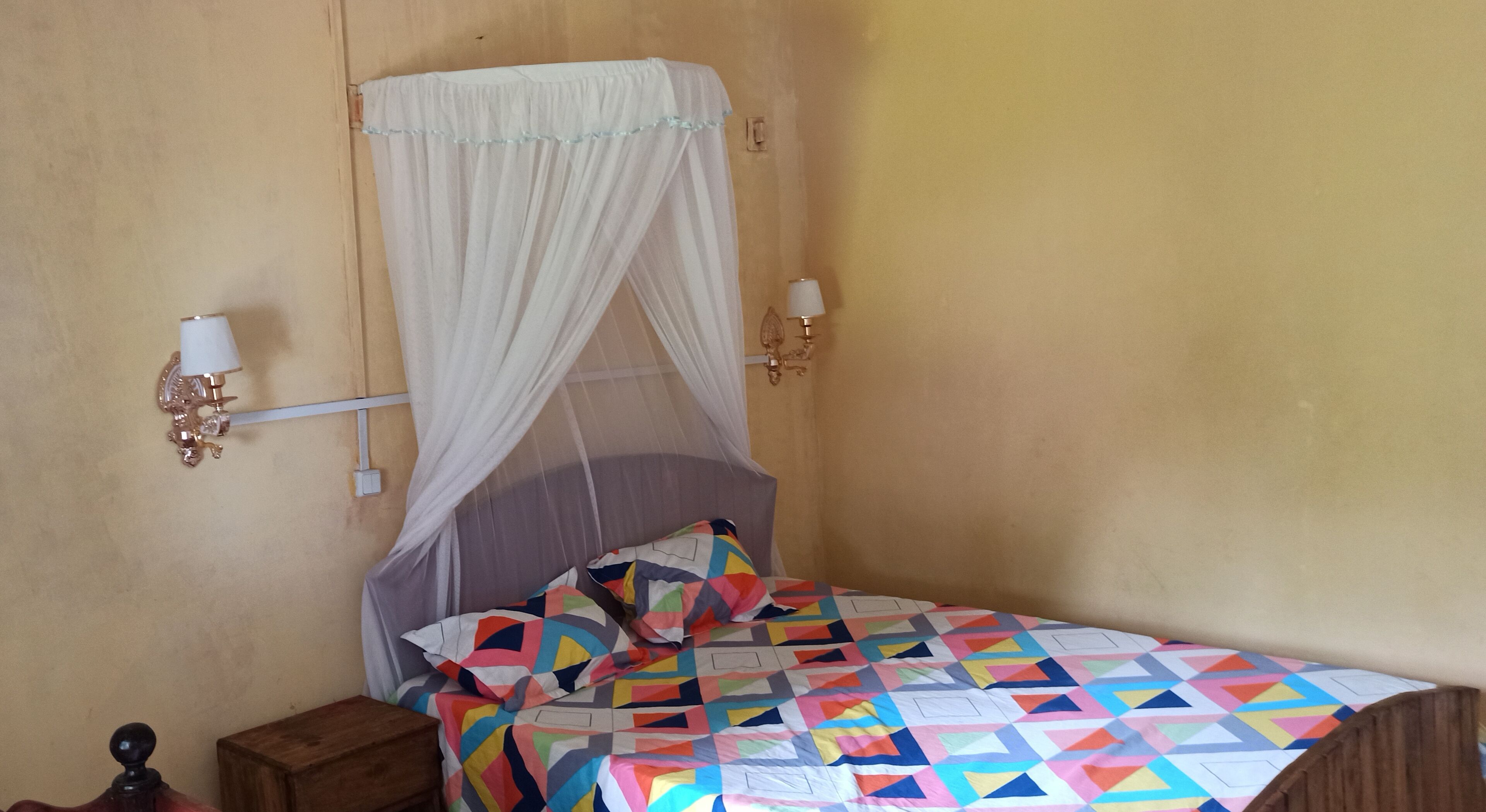 Una cama con un colcha de colores, un dosel y lámparas fijadas a la pared.