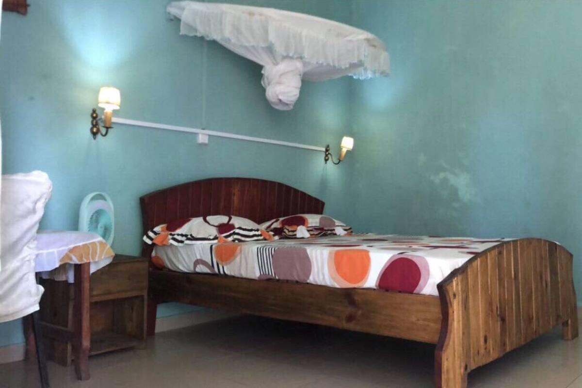 Um quarto com uma cama de madeira, uma mesinha de cabeceira, uma prateleira na parede e uma luminária de parede.