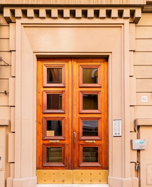 Una puerta doble de madera con paneles de vidrio y manijas de bronce, integrada en la fachada de un edificio color beige.
