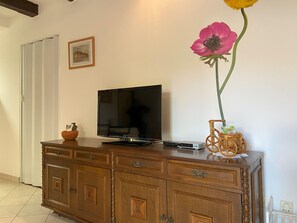 A wooden cabinet with a flat-screen TV, a small basket, and a vase with a single flower.
