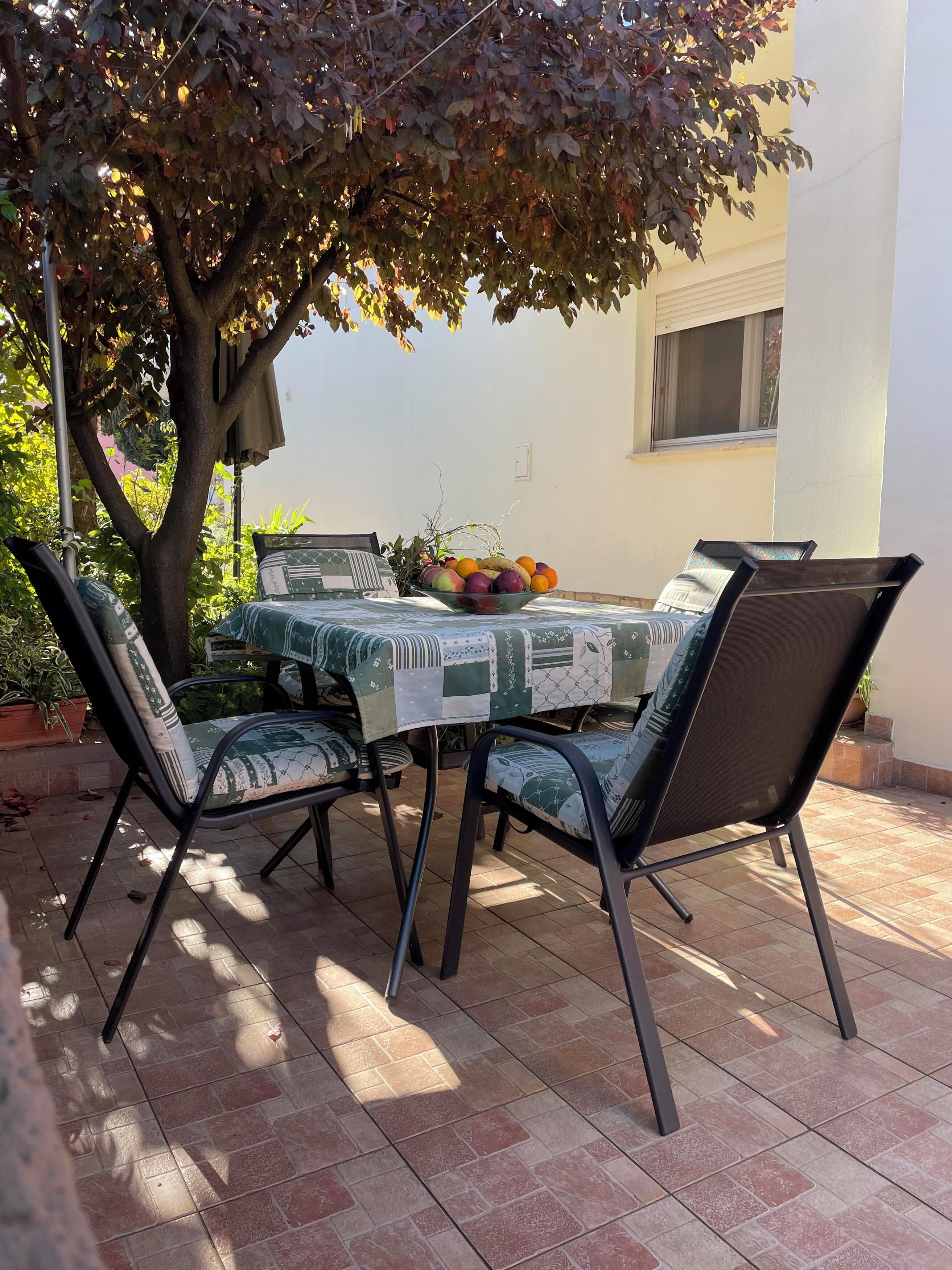 Eine Terrasse im Freien mit einem für zwei Personen gedeckten Tisch, umgeben von Stühlen, unter einem Baum.