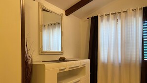 A bathroom with a white vanity, a mirror, and a window with white curtains. - Apartment Ivan (Rovinj)