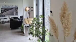 Un salon moderne avec un canapé, une table basse et un coin repas avec des chaises. On y trouve également des plantes et une lampe.