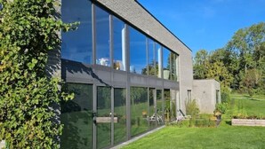 Un bâtiment moderne doté de grandes fenêtres en verre, d’une pelouse bien entretenue et d’un espace jardin agrémenté de plantes et d’un banc.