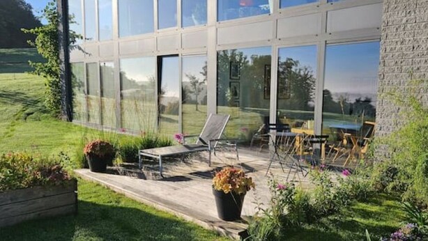 Un patio extérieur moderne doté d’un mur de verre, d’une terrasse en bois et d’un espace détente avec des chaises et une table.