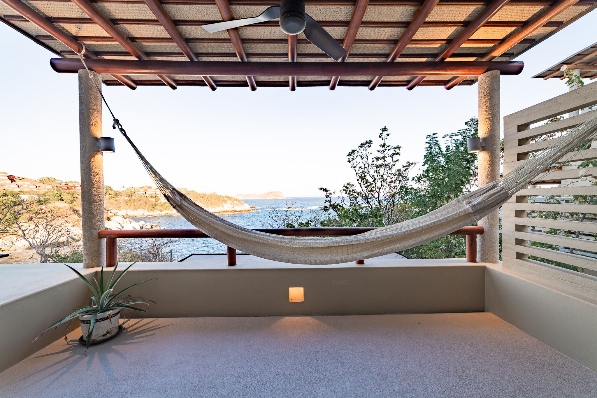 A hammock under a pergola with a view of the sea and hills.