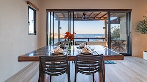 A dining area with a table set for two, large windows, and a view of the sea. - Oceanfront Residence with Beach Access (Huatulco)