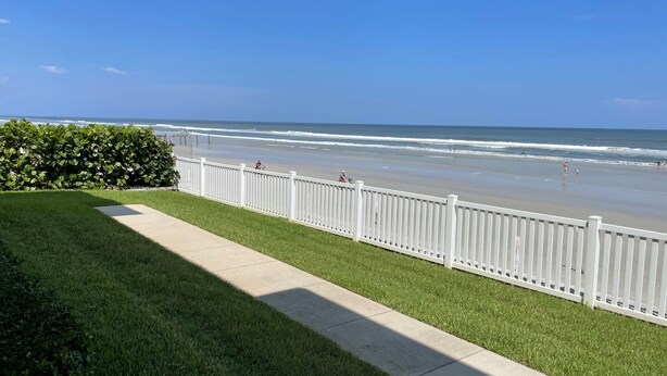 A grassy area with a white fence leading to a beach. - Ground Floor Direct Oceanfront 2/2 (New Smyrna Beach)